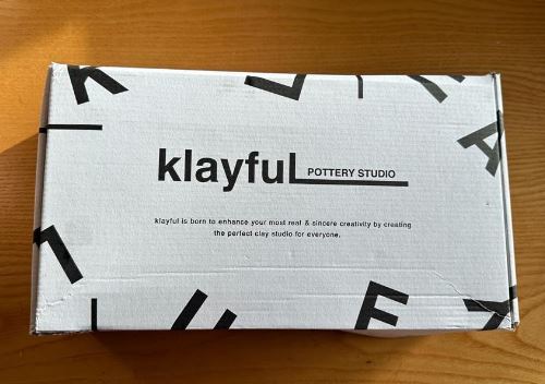 Geschlossene Verpackung des Klayful Pottery Studios auf einem Holztisch mit dem Slogan 'Klayful is born to enhance your me-time & enforce creativity by creating the perfect clay studio for everyone